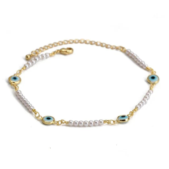 Gold and pearl bracelet with blue evil eye charms on white background