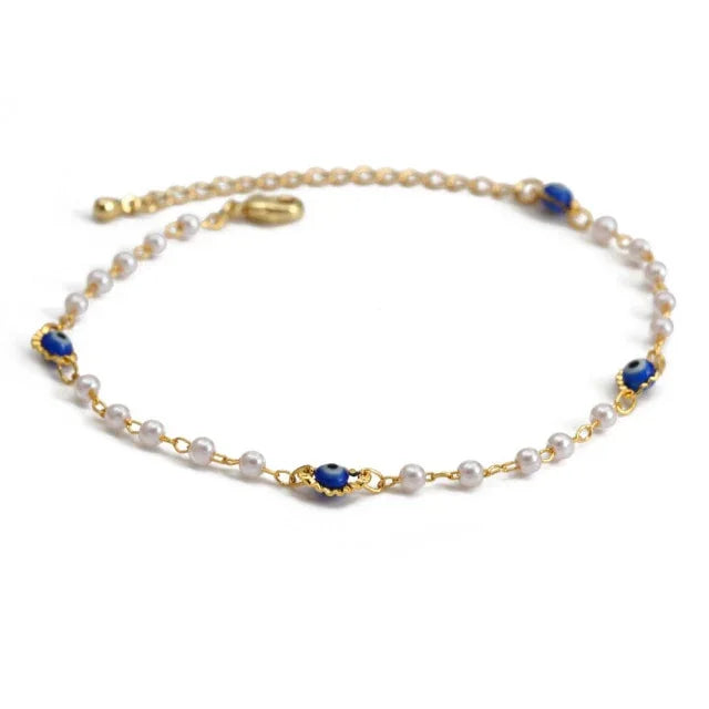 Gold bracelet with white pearls and blue evil eye charms on a white background