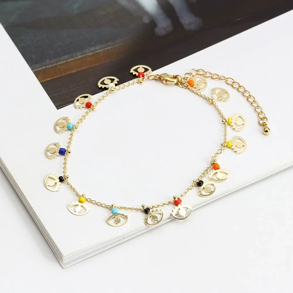 Gold chain bracelet with colorful beads and small eye-shaped charms on a white background.